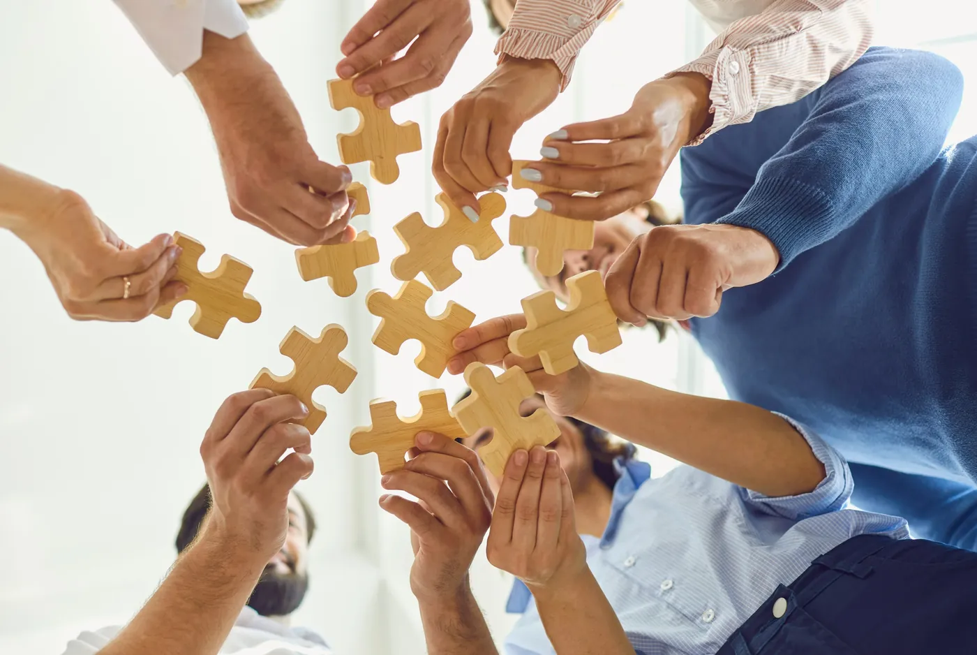 Several people holding wooden puzzle pieces together, representing a collaborative approach to change