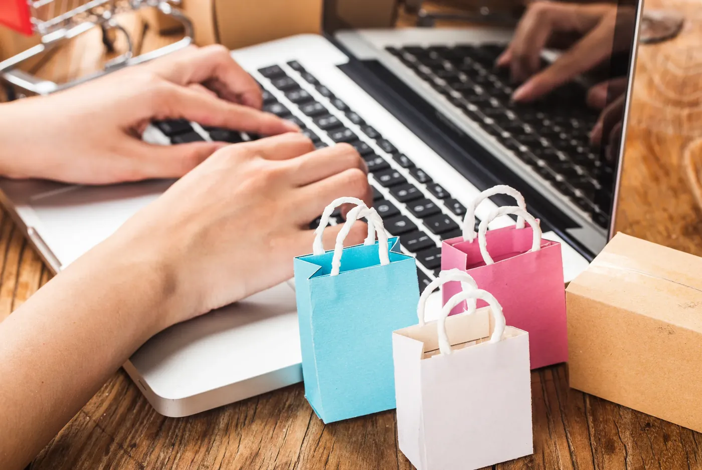 Hands resting on a laptop keyboard beside small paper shopping bags, representing a considered online purchase